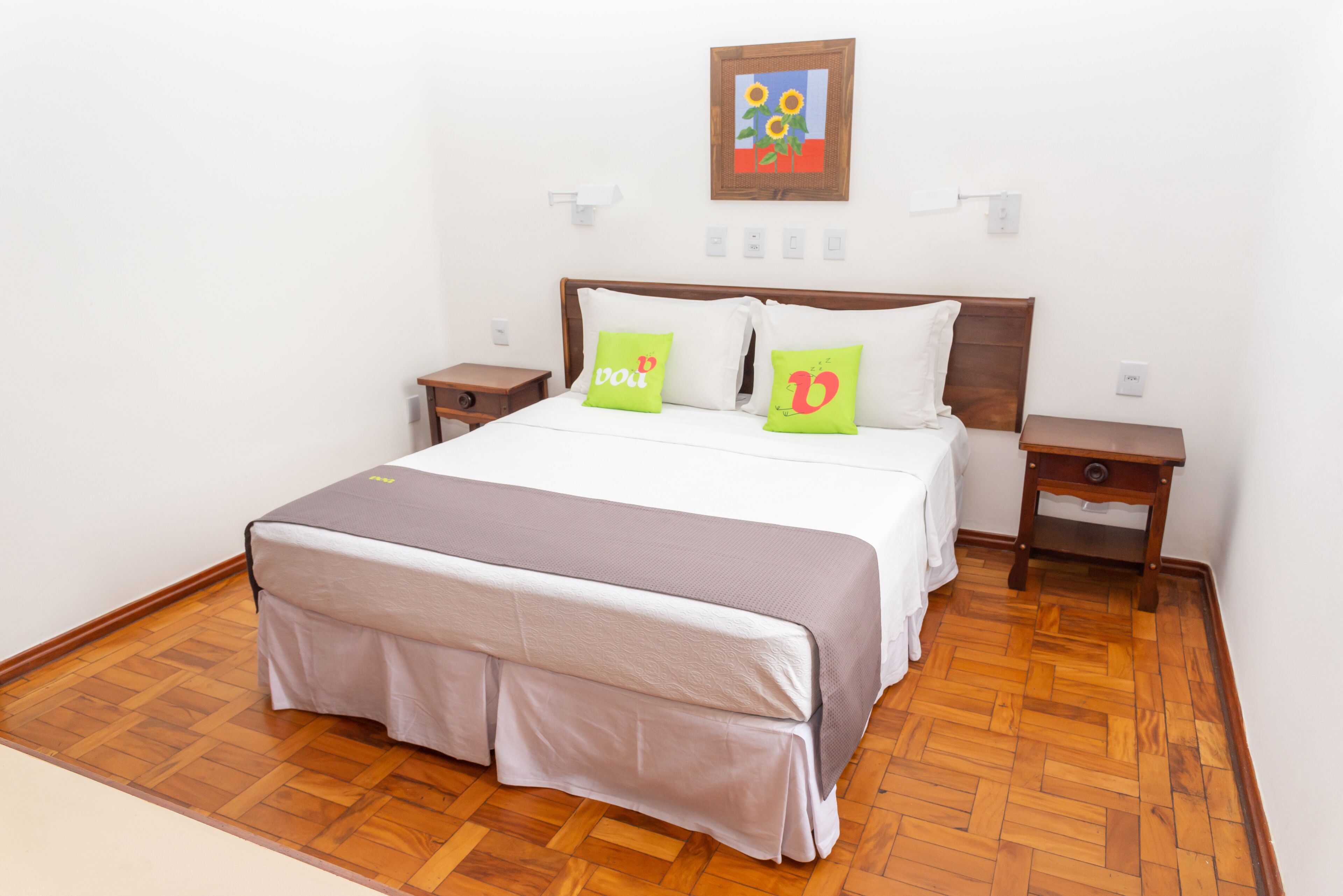 Une chambre à coucher bien aménagée, avec un grand lit, deux tables de chevet, une œuvre d’art accrochée au mur et un plancher en parquet.