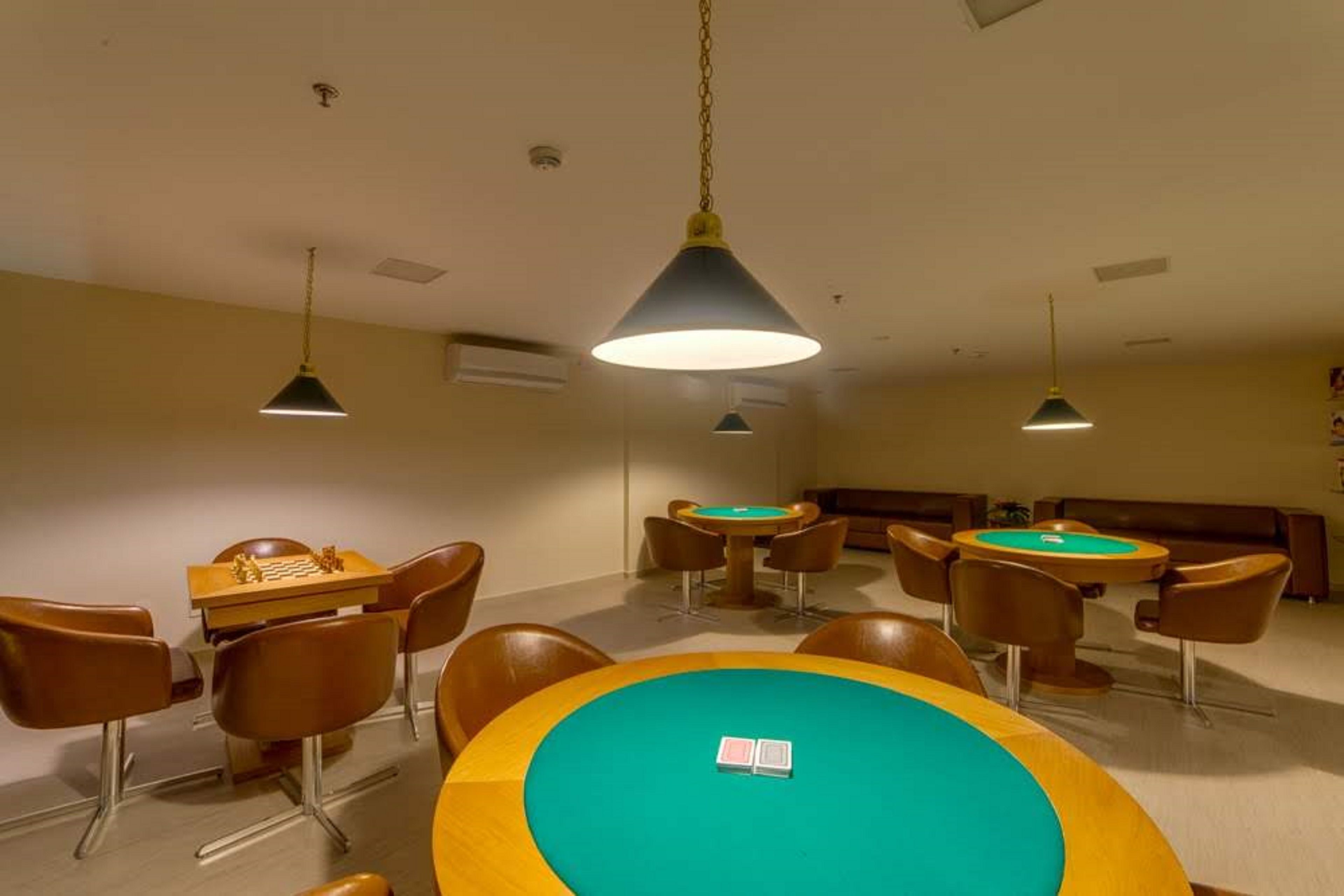 Una habitación con varias mesas y sillas, algunas con tapetes de fieltro verde, y una mesa central grande con una fichas de póquer blancas.