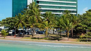 Un hotel moderno con fachada de vidrio, situado cerca de una playa con palmeras.