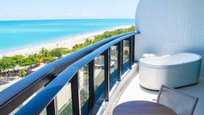 Un balcón con vista a una playa, una bañera y una mesa con una silla.