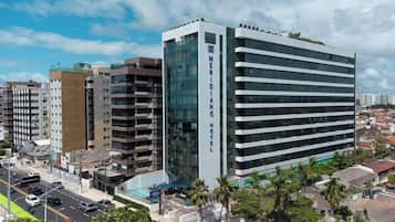 Un hotel moderno con fachada de vidrio y varios pisos, rodeado de otros edificios bajo un cielo despejado.