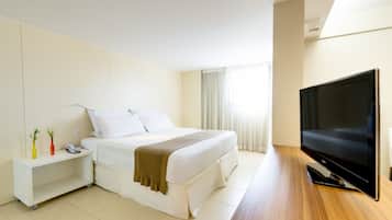 Una habitación de hotel con cama, televisión, mesita de noche y una pequeña estantería decorada.