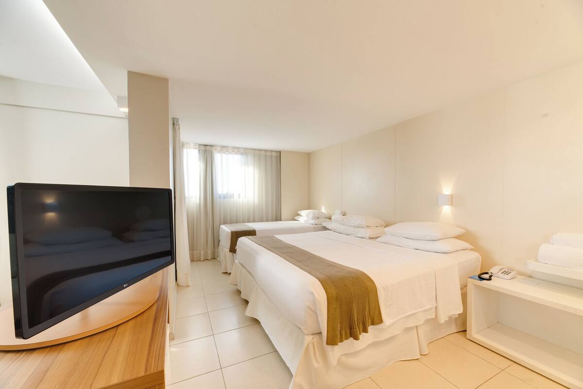 A hotel room with a flat-screen TV, two beds, a bedside table with a phone, and a window with curtains.