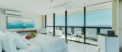 A modern bedroom with a large bed, a desk, and a view of the sea.