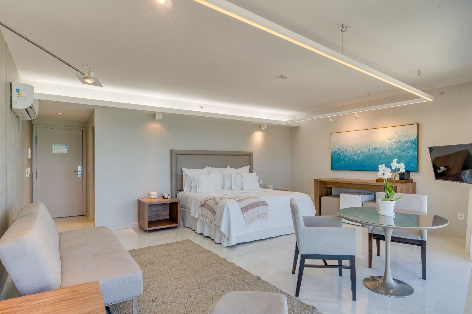 Una habitación de hotel moderna con una cama grande, una zona de estar con mesa y sillas, un escritorio y un cuadro en la pared.