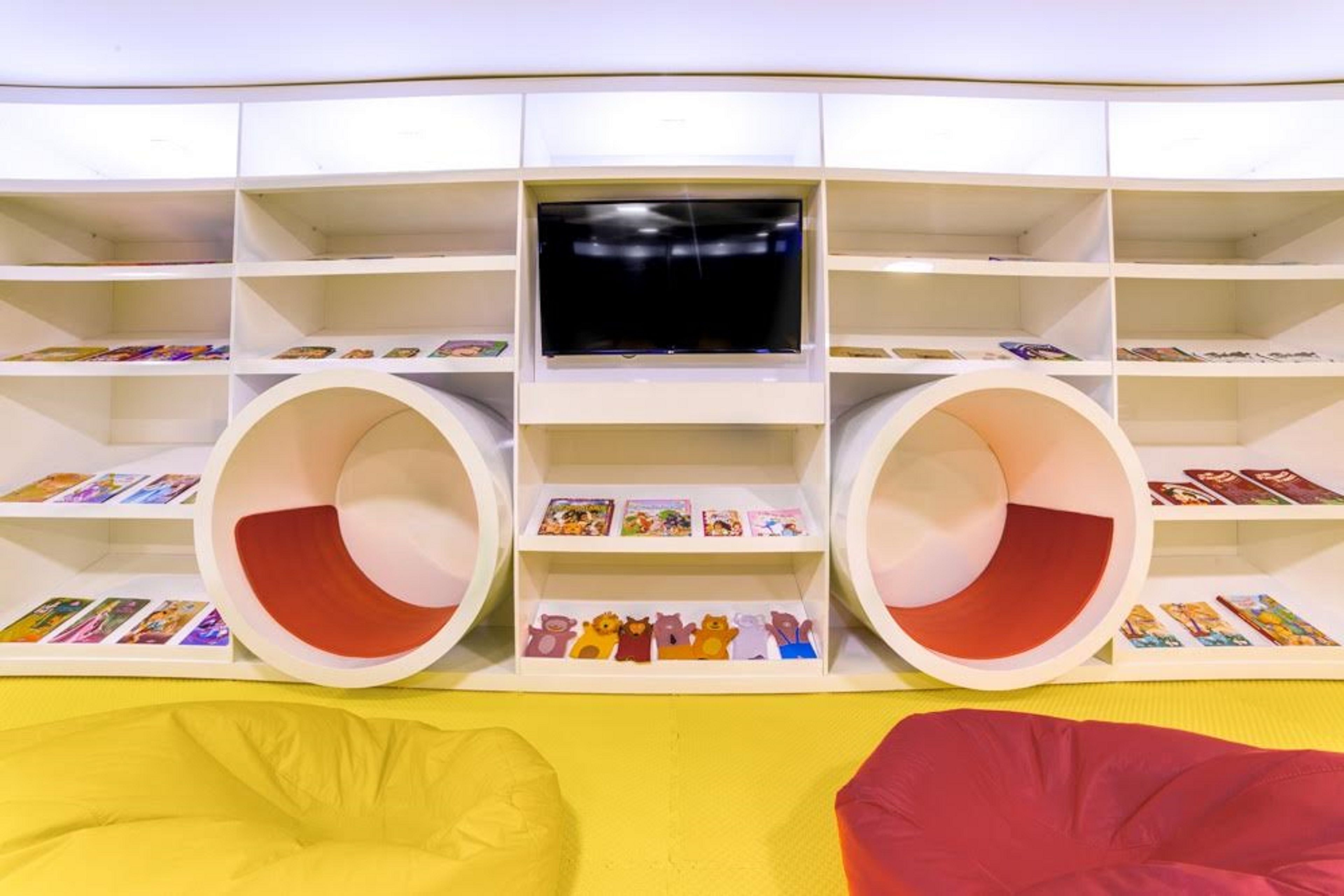 Zona infantil con televisor, estanterías y dos amplias áreas de asientos circulares.