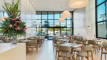 Um restaurante espaçoso com pé-direito alto, grandes janelas e iluminação pendente moderna.