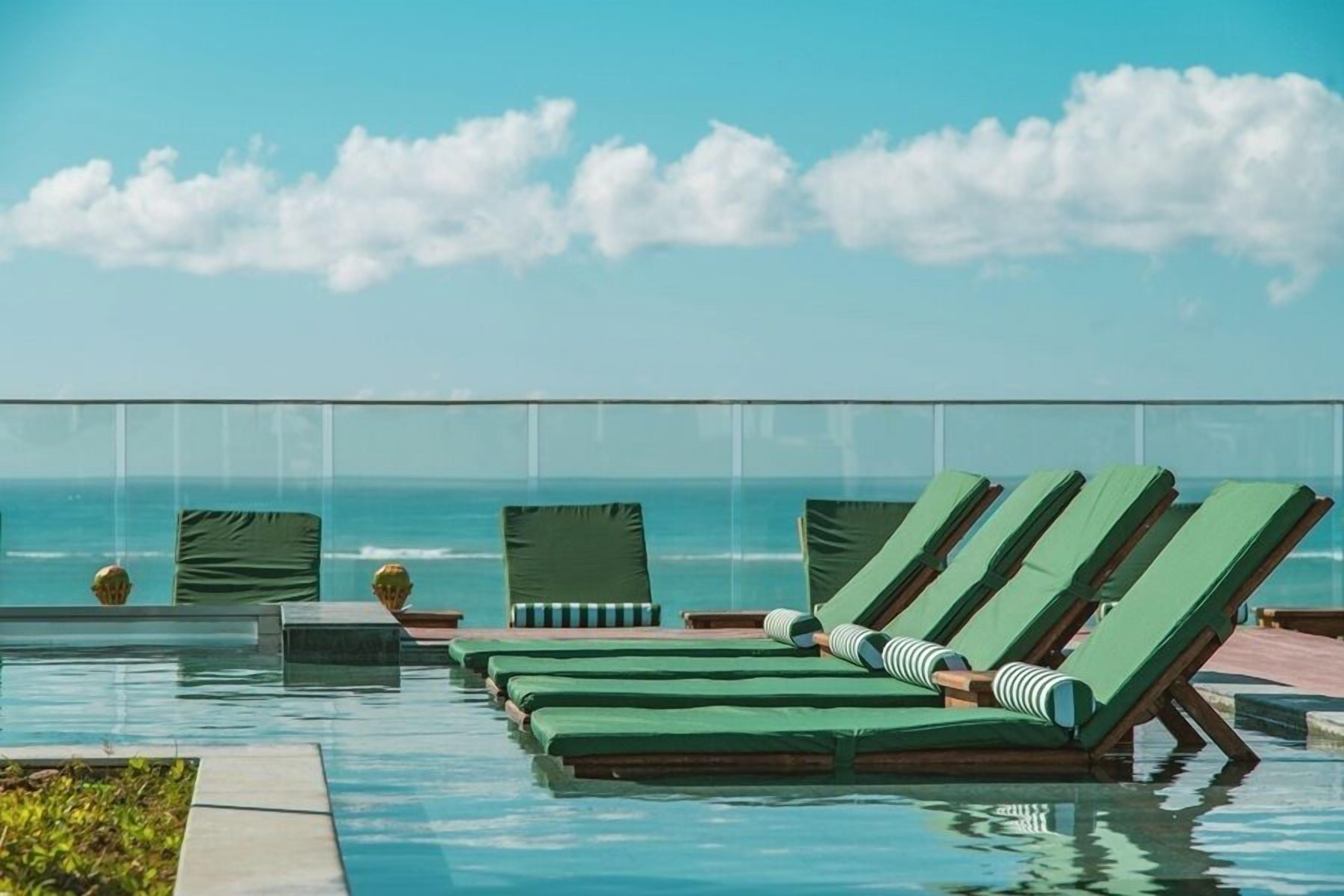 A poolside area with lounge chairs and a view of the ocean.
