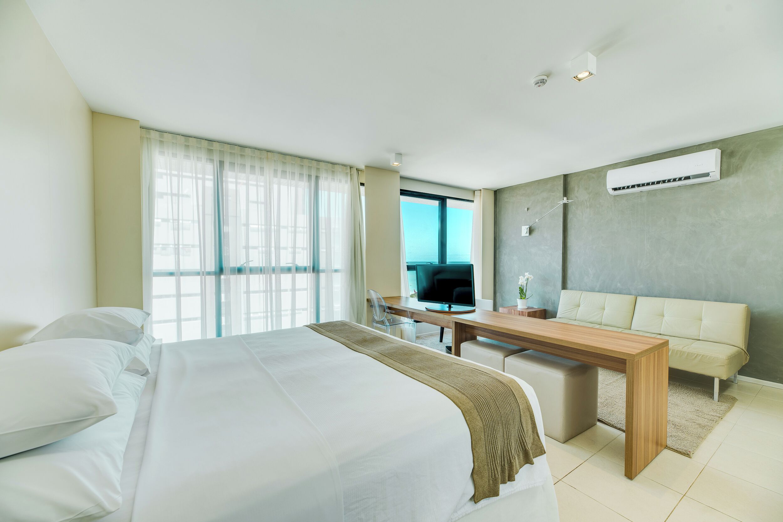 Habitación de hotel moderna con una cama grande, un escritorio, un sofá y un equipo de aire acondicionado.