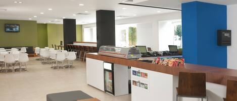 A modern cafe with a long counter, bar stools, and a seating area with tables and chairs.