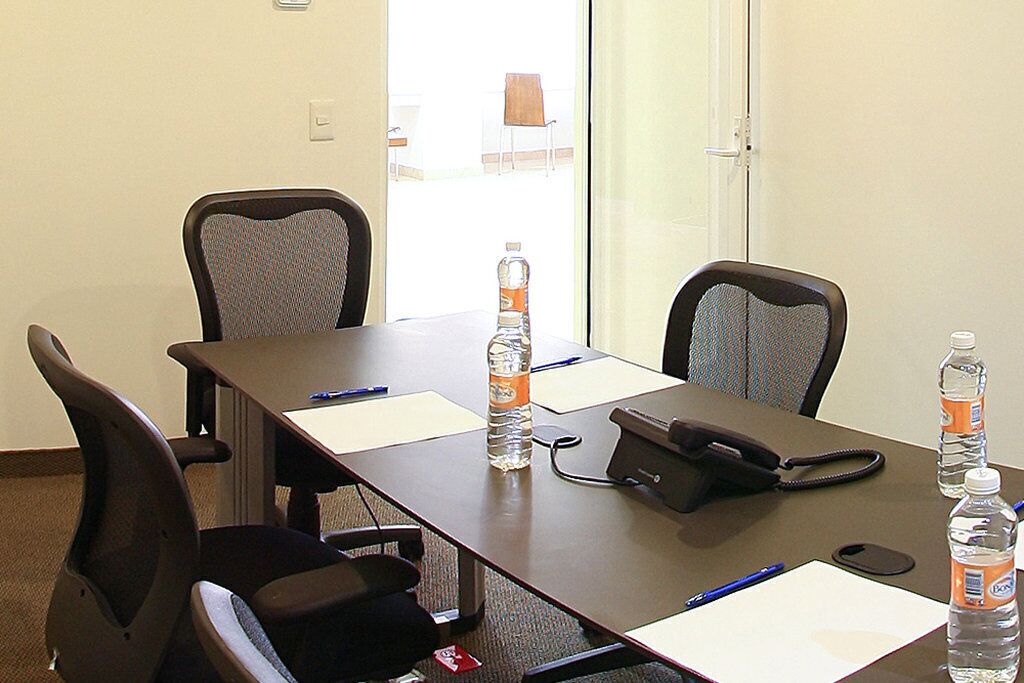 Une salle de conférence avec une longue table, quatre chaises, des bouteilles d’eau, un téléphone et des documents.