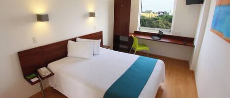 A hotel room with a bed, bedside table, desk, chair, and a window with a view.