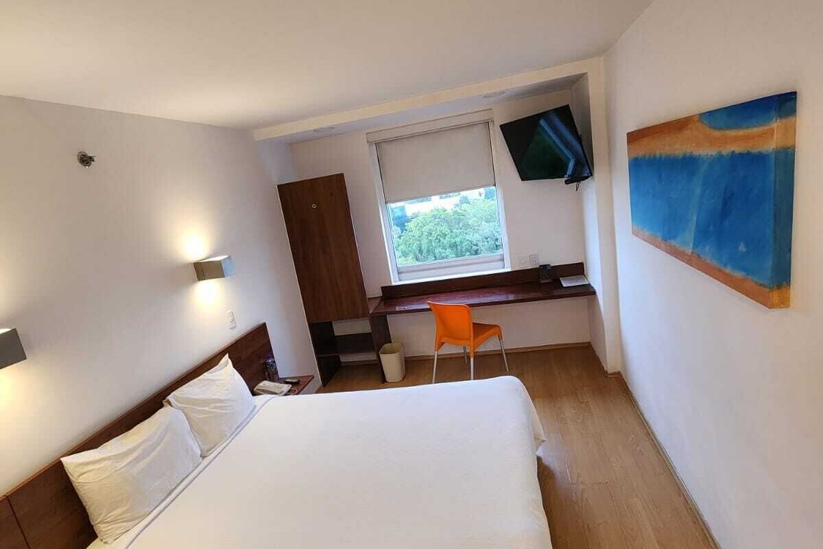 Una habitación de hotel con cama, escritorio, silla, televisor y ventana.