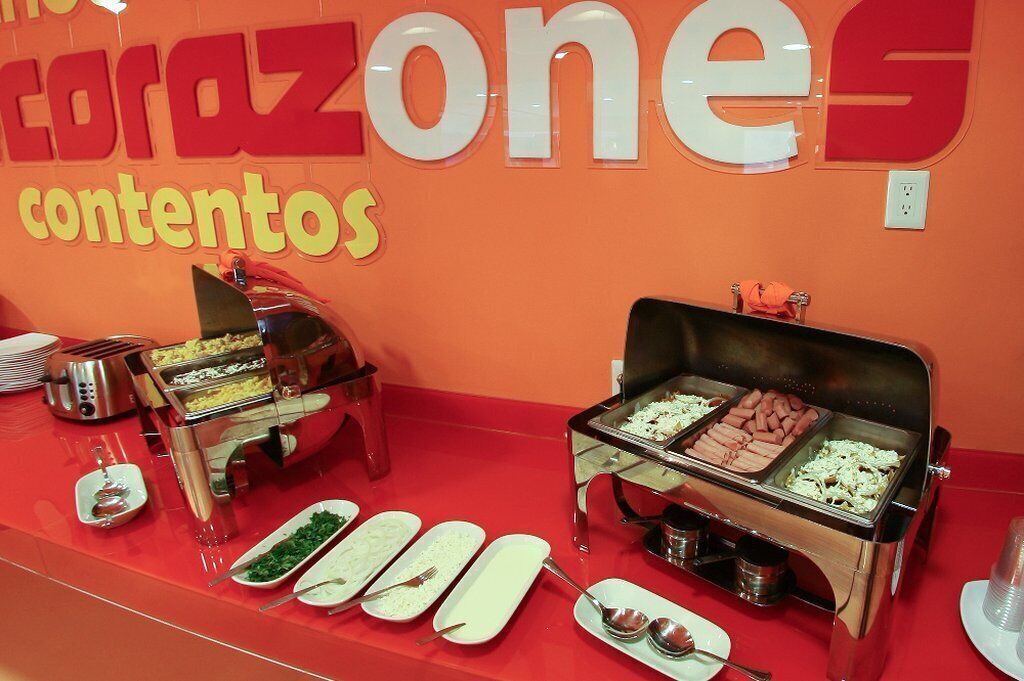 A buffet setup with various food items and utensils on a red table, with a sign reading "corazon contents" in the background.