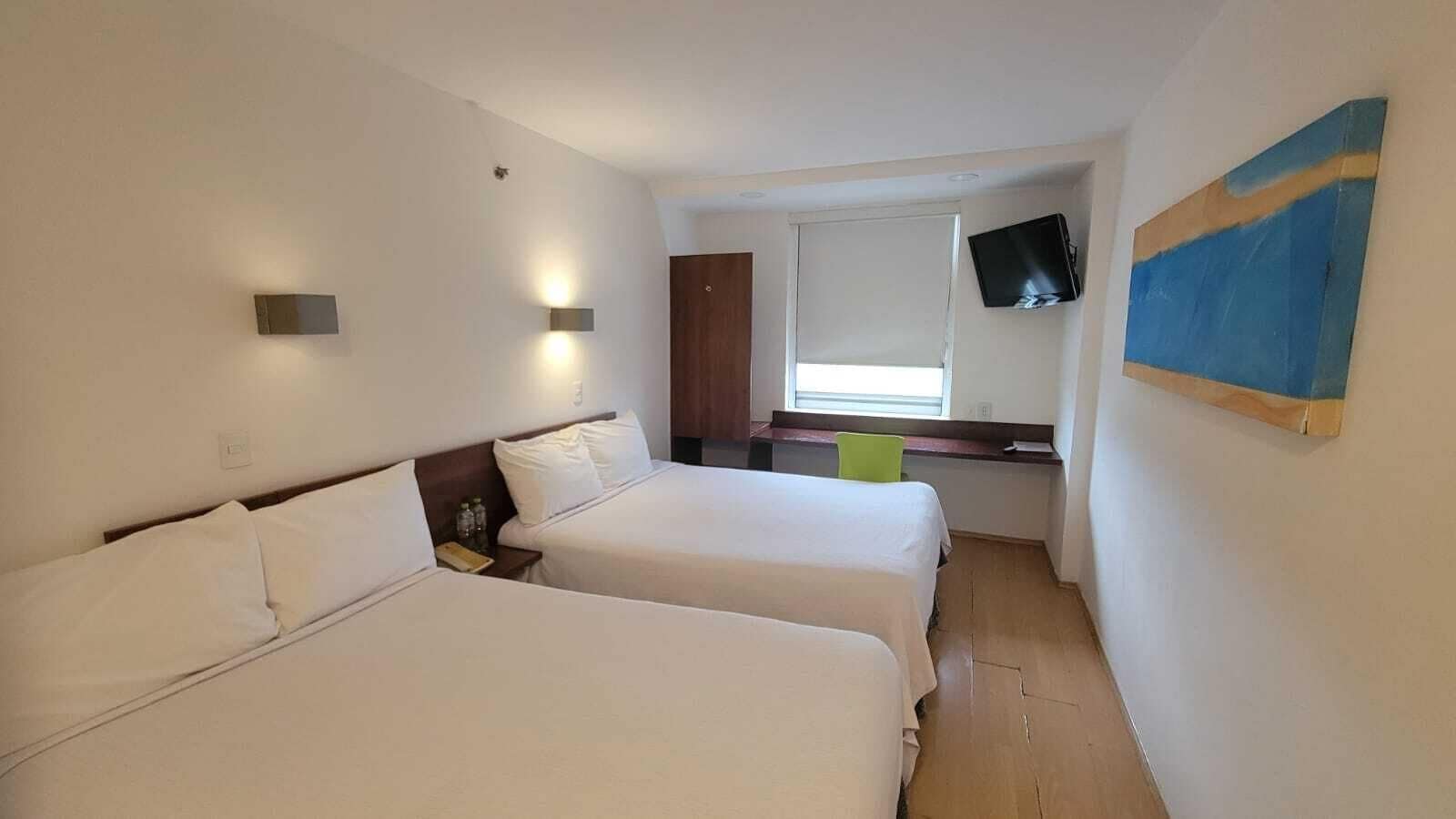 A hotel room with two beds, a television mounted on the wall, and a painting.