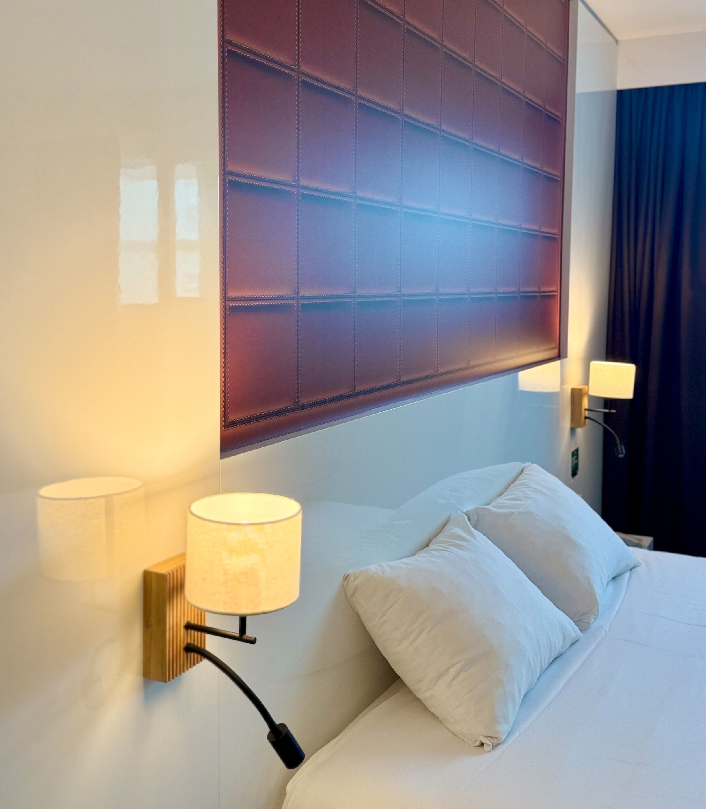 A hotel room with a large bed, two wall-mounted lamps, and a padded headboard.