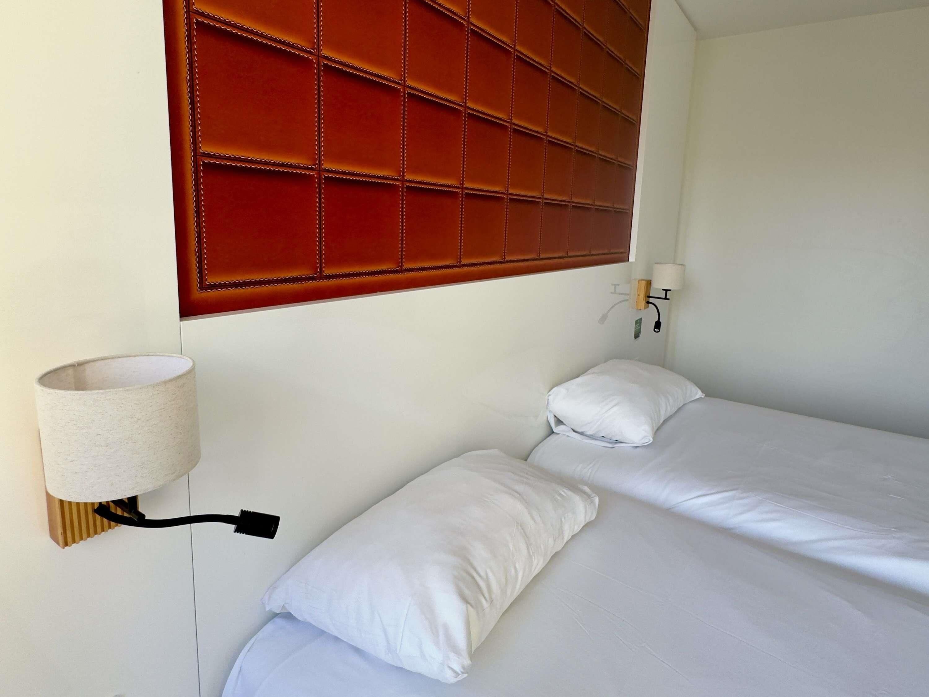 Een hotelkamer met een hoofdeinde, twee bedden, een wandlamp en een nachtkastje.