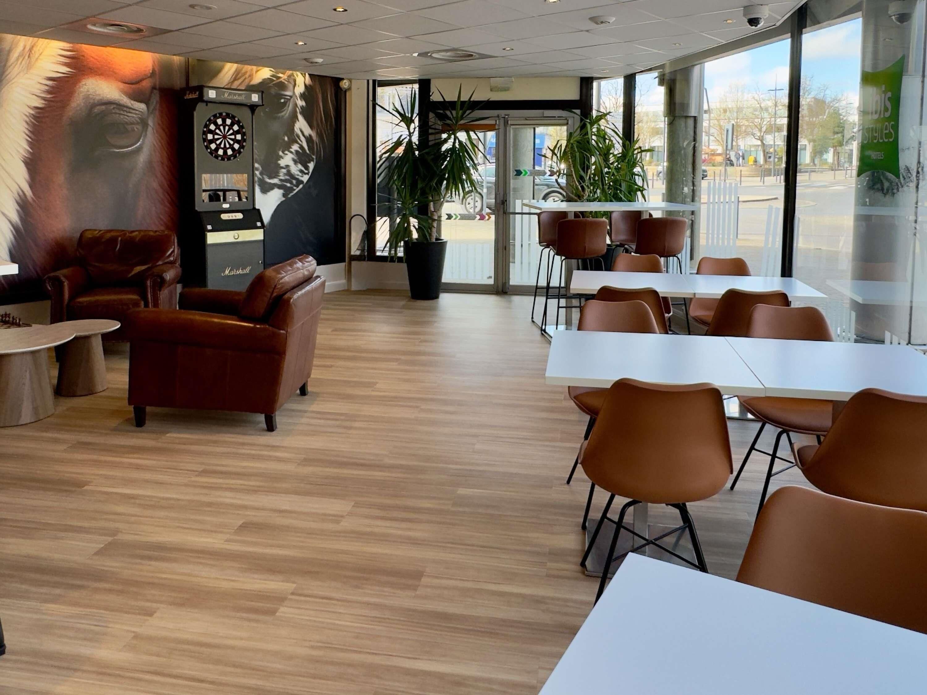 A modern restaurant interior with leather seating, a dartboard, and a large window offering a view of the street.