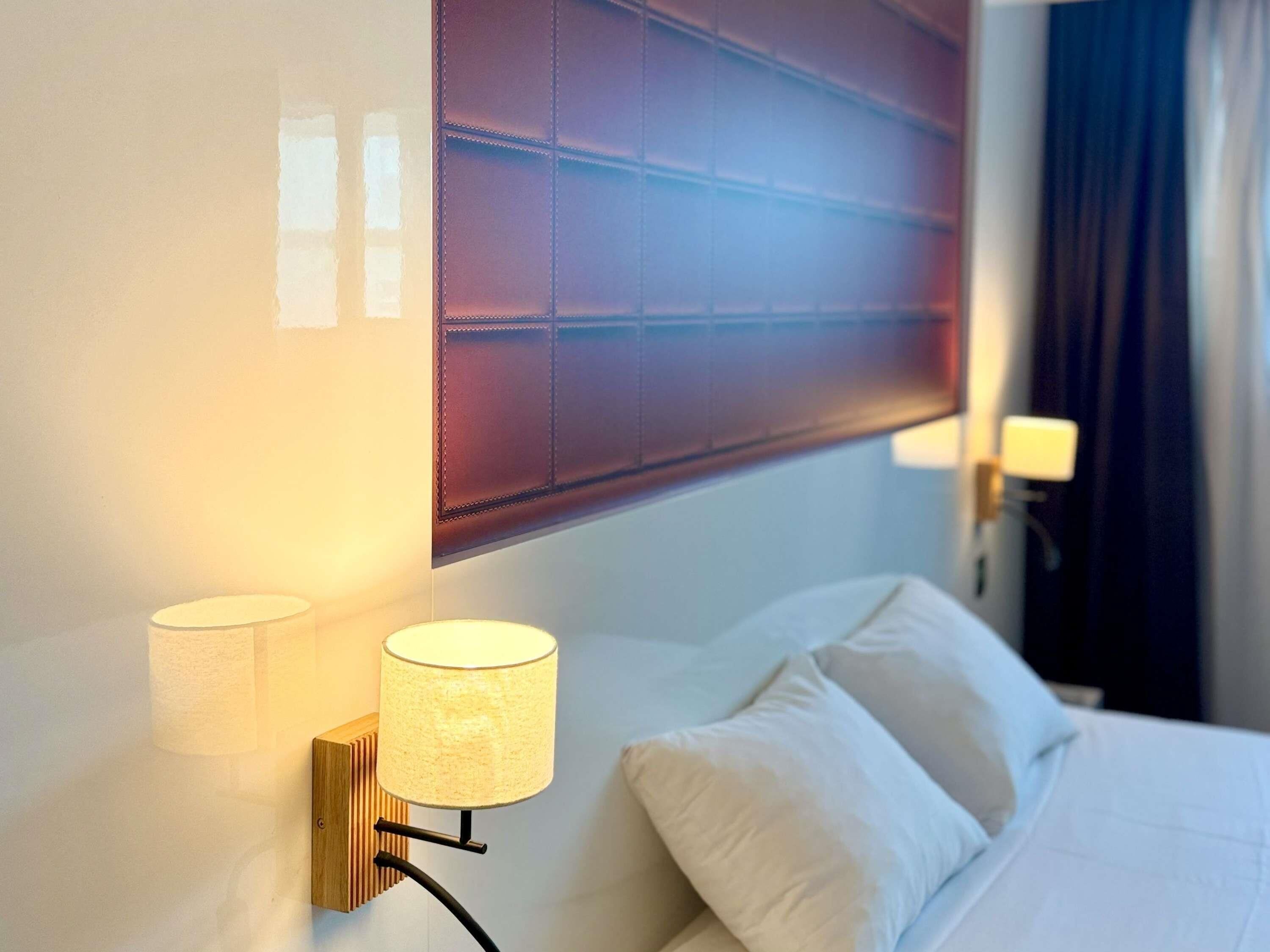 Una habitación de hotel con una cama, un cabecero y una lámpara fijada a la pared.