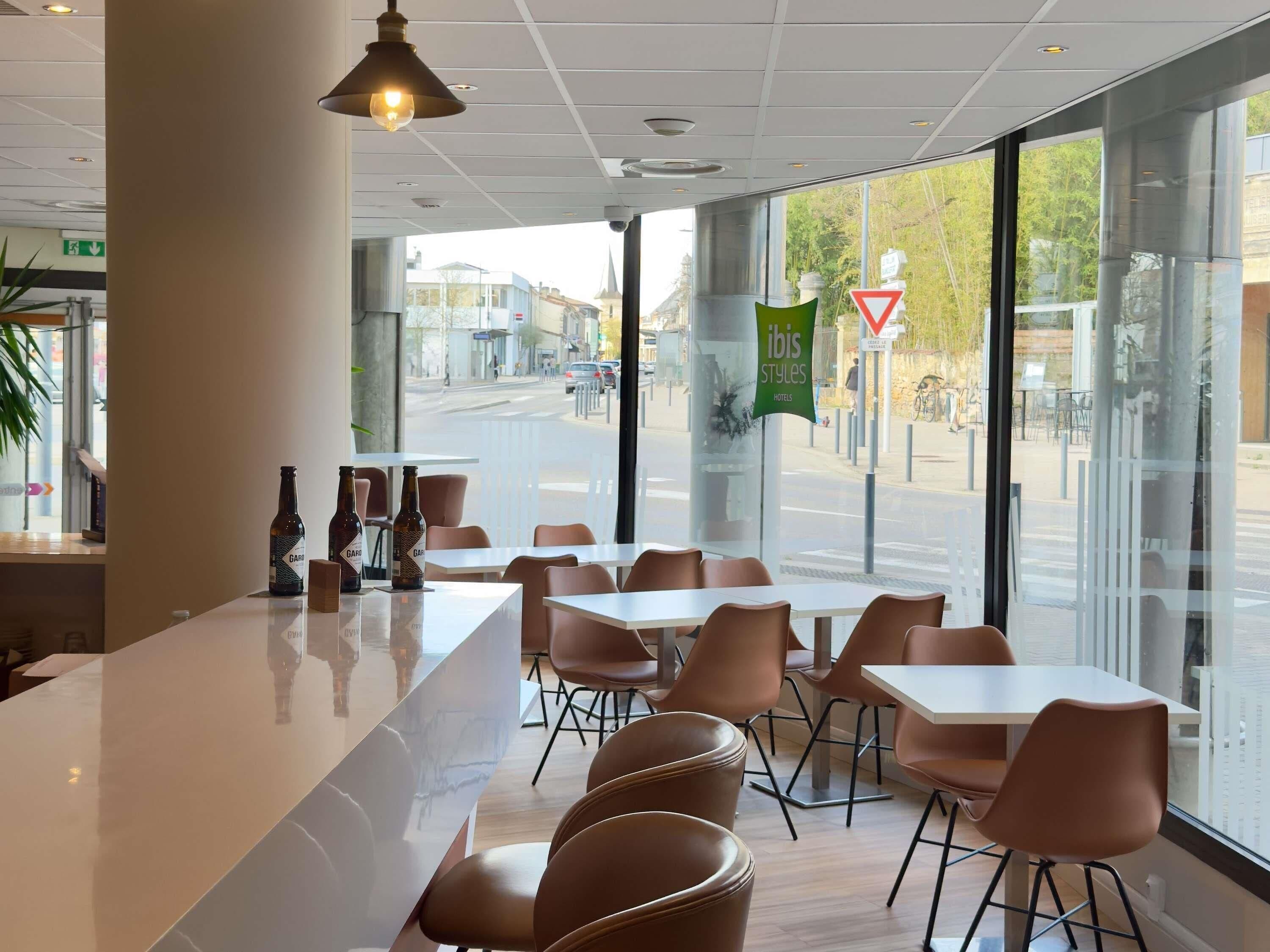 A modern restaurant with a bar area, large windows, and a view of the street.