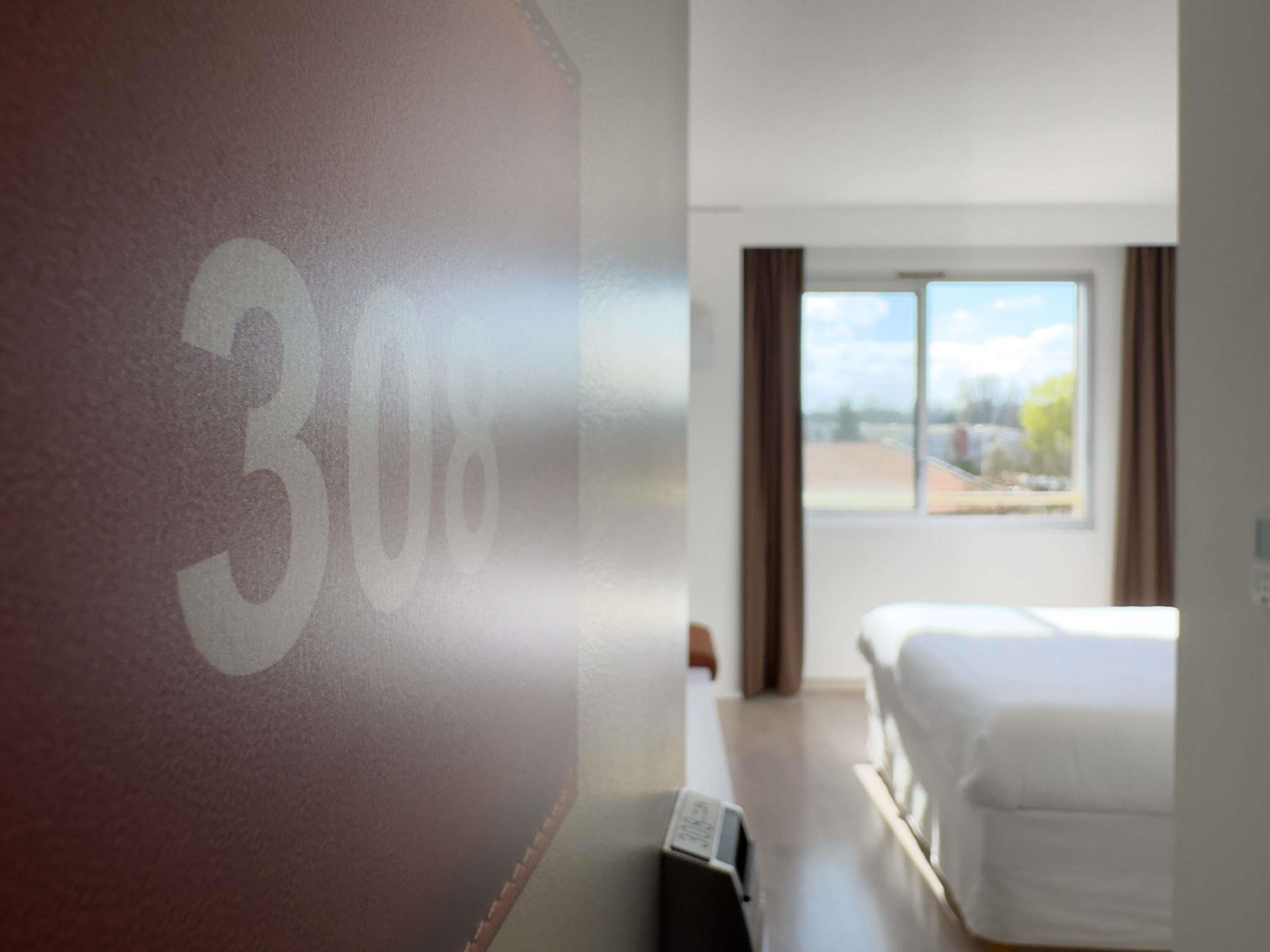 A hotel room with a bed, a window, and a wall with a number.