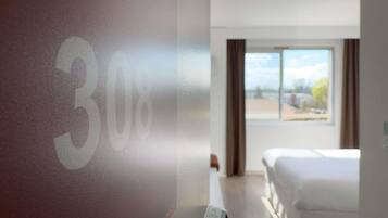 A hotel room with a bed, a window, and a wall with a number.