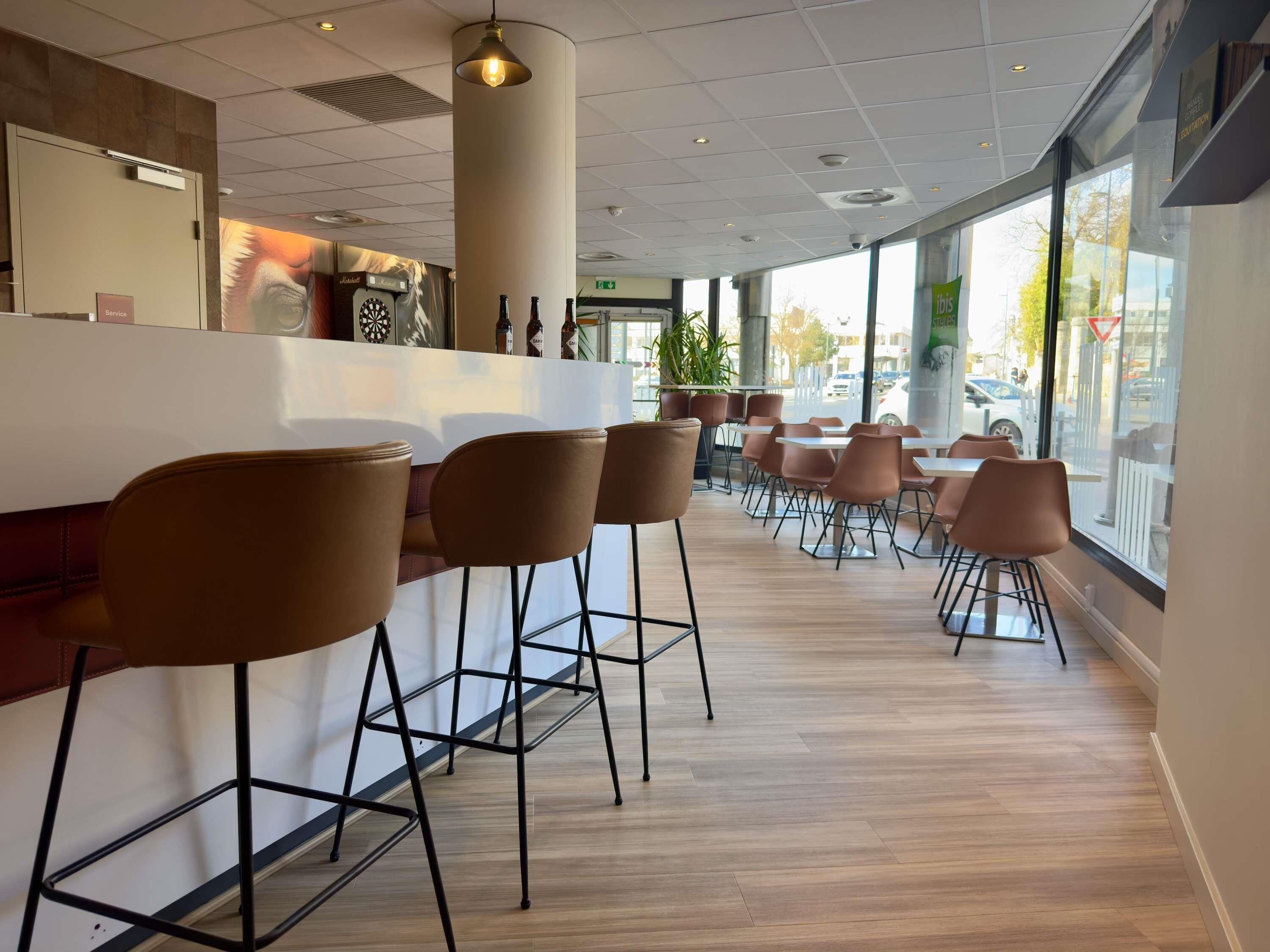 A modern bar area with high stools, a counter, and large windows offering a view of the street.