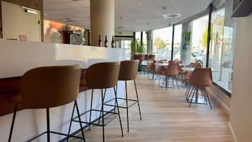 A modern bar area with high stools, a counter, and large windows offering a view of the street.