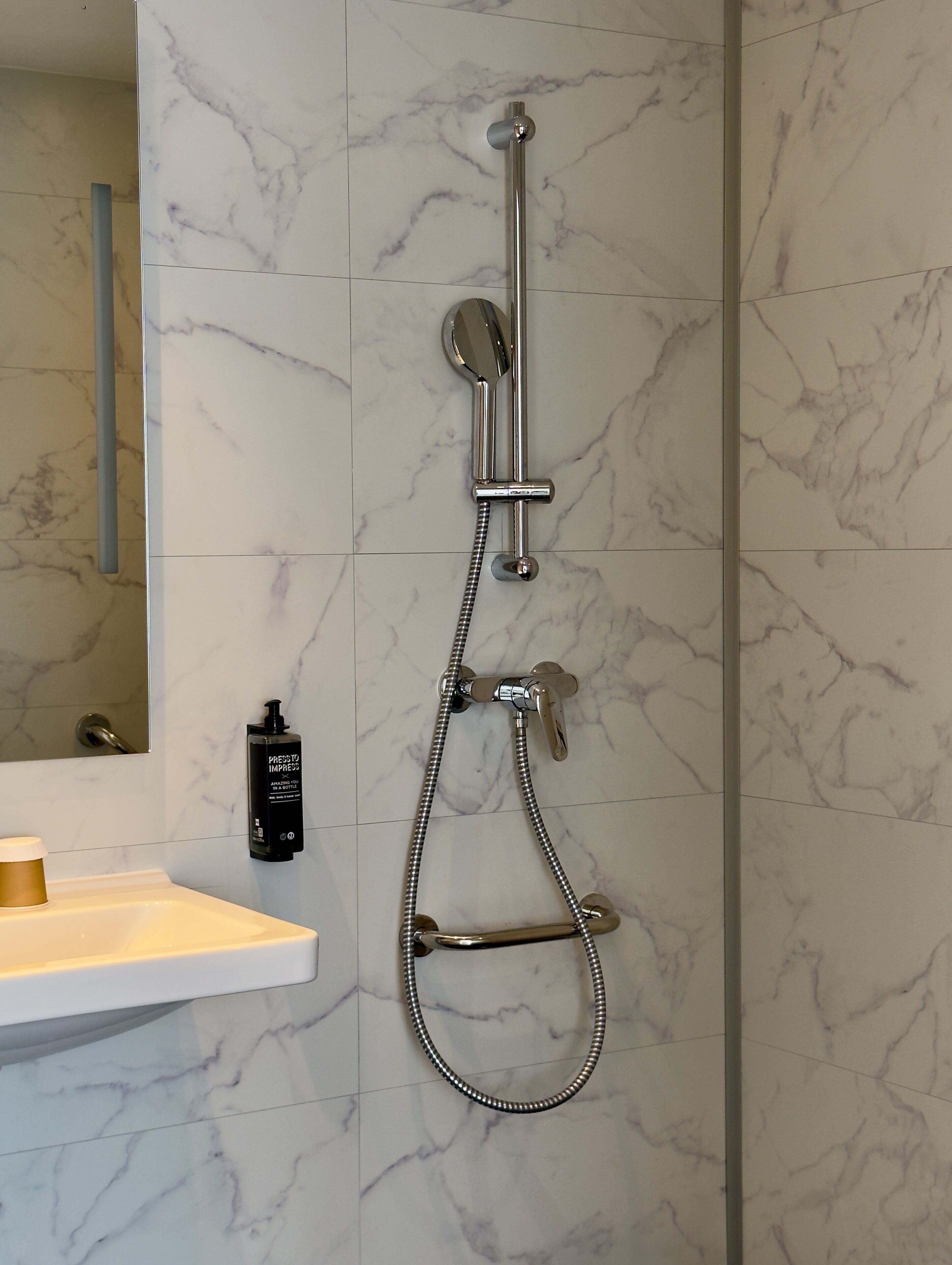 A bathroom with a shower, a sink, and a bottle of shampoo.
