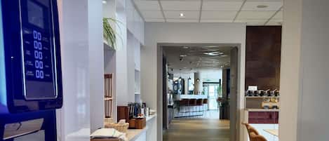 Un intérieur moderne comprenant un comptoir d’accueil, un espace café et un coin salon.
