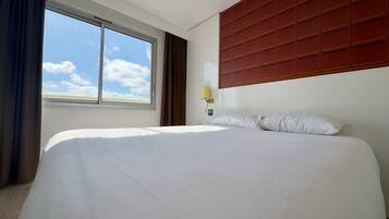Hotelkamer met een groot bed, een raam met gordijnen, een wandlamp en uitzicht op de lucht.