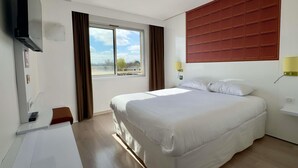 A hotel room with a bed, a desk, a TV, a window with curtains, and a wall-mounted light fixture. - ibis Styles Bordeaux Saint Médard (Saint-Medard-en-Jalles)