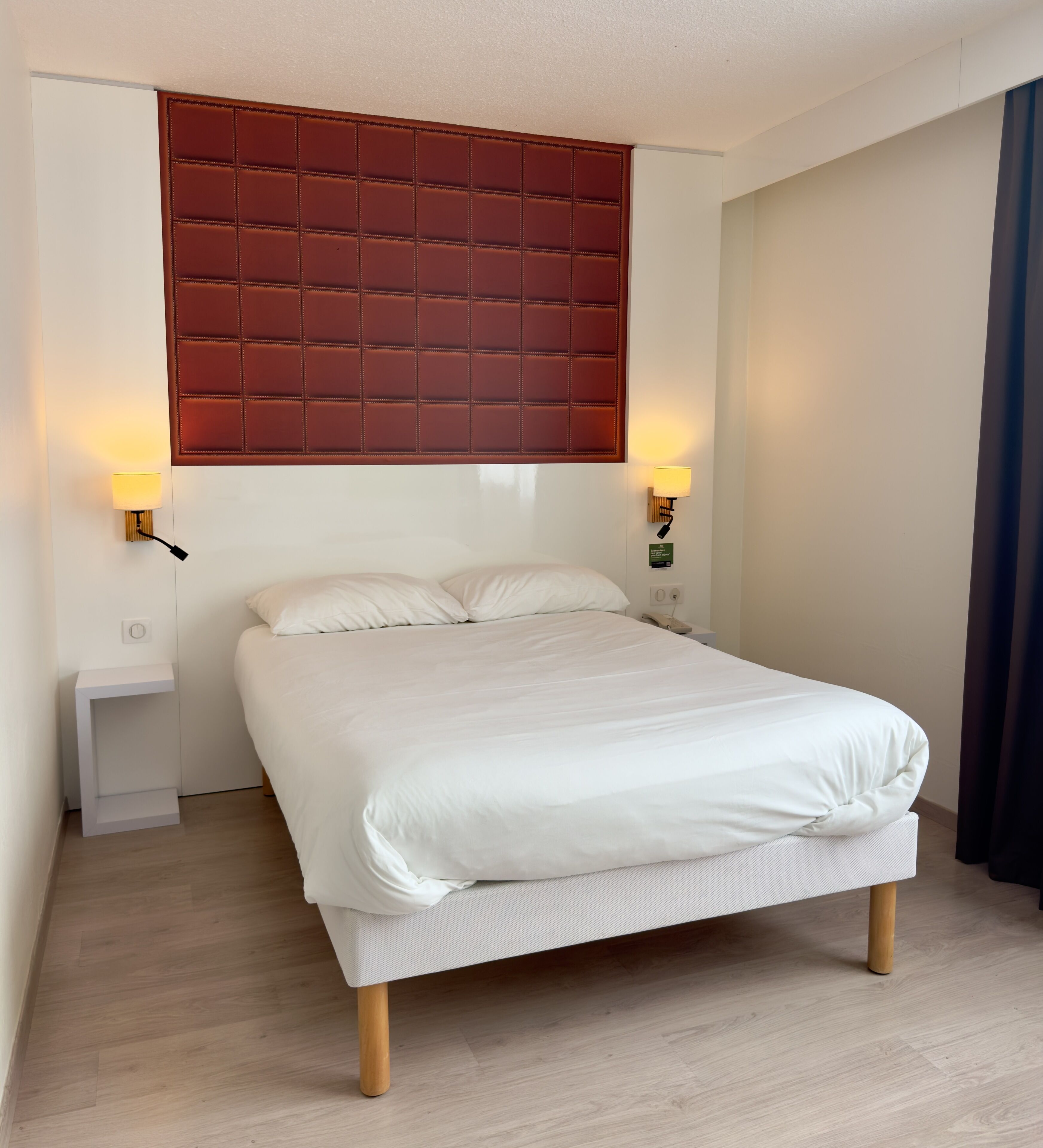 Una habitación de hotel con una cama, dos lámparas de noche, una mesita de noche y un cabecero rojo.