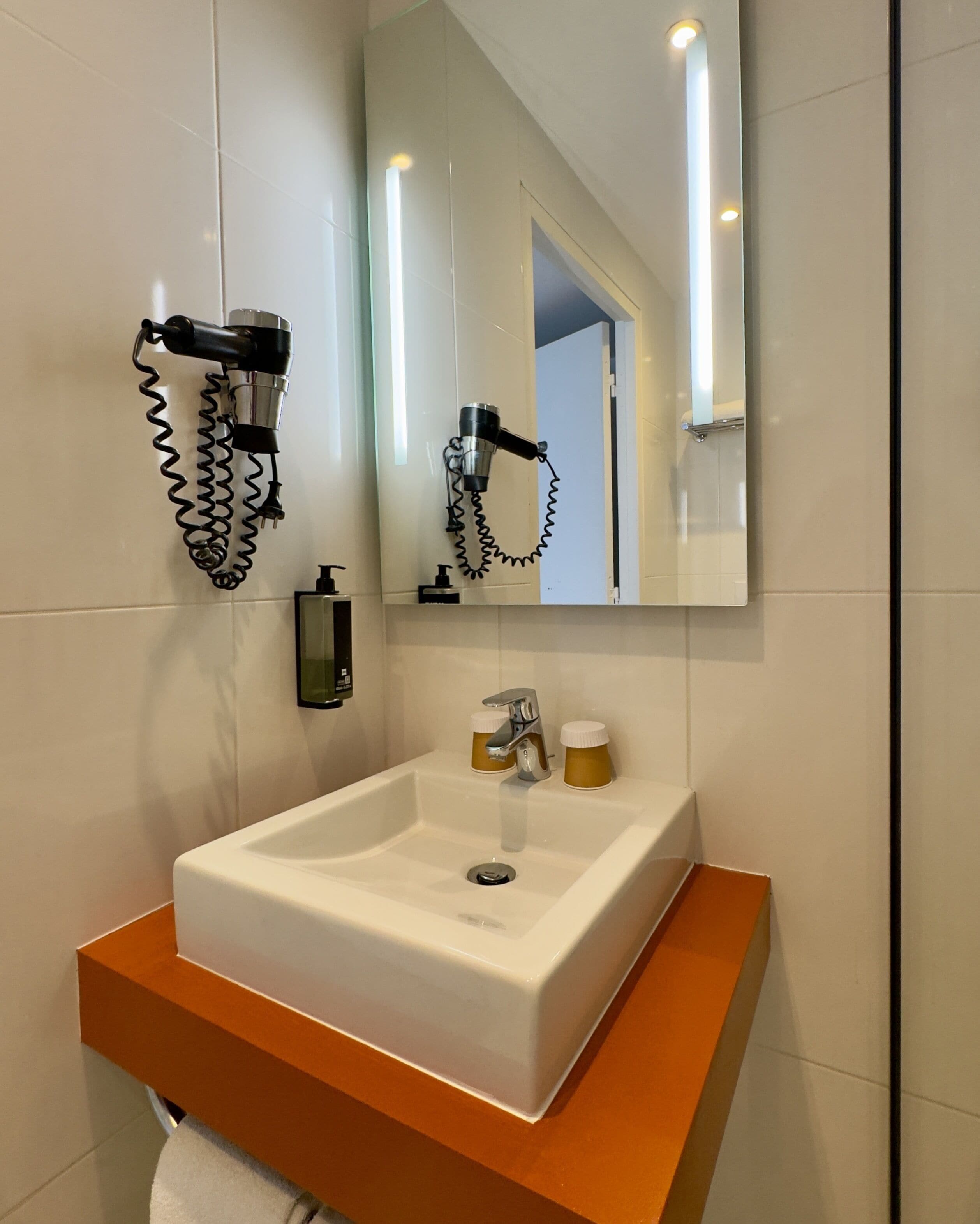 A bathroom with a white sink, a mirror, and a hairdryer mounted on the wall.