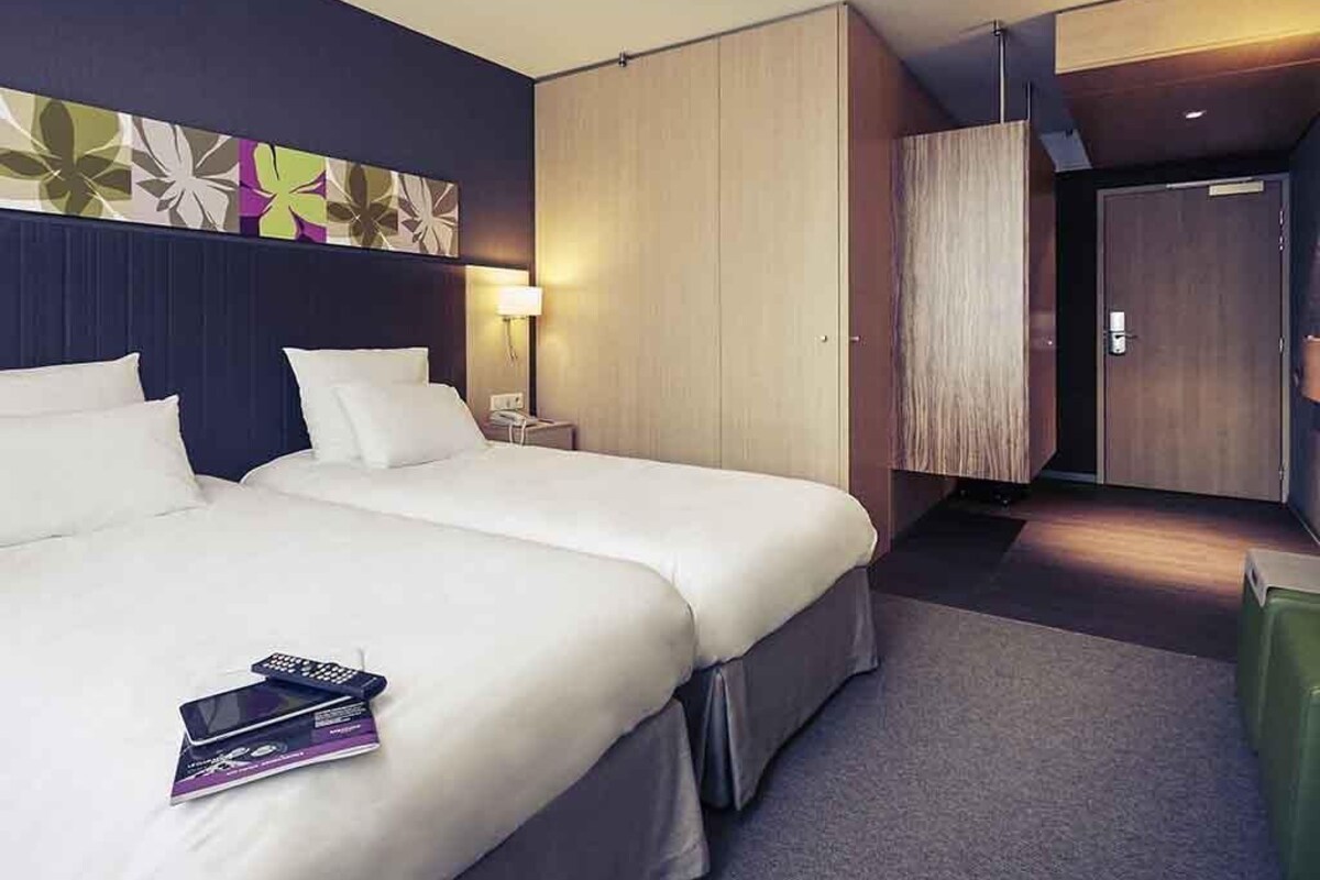 Een hotelkamer met twee bedden, een nachtkastje, een lamp, een kledingkast en een deur.