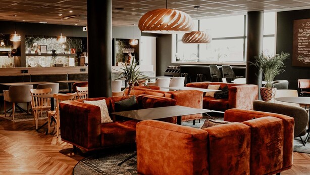 Un espace de détente moderne avec des canapés orange, des tables en bois et un parquet en bois disposé en chevrons.