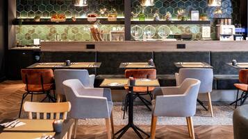 A modern restaurant interior with hexagonal patterned walls, cushioned seating, and a bar area with various food items and glassware.
