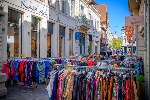 Een straat met een kledingmarkt en diverse winkels.