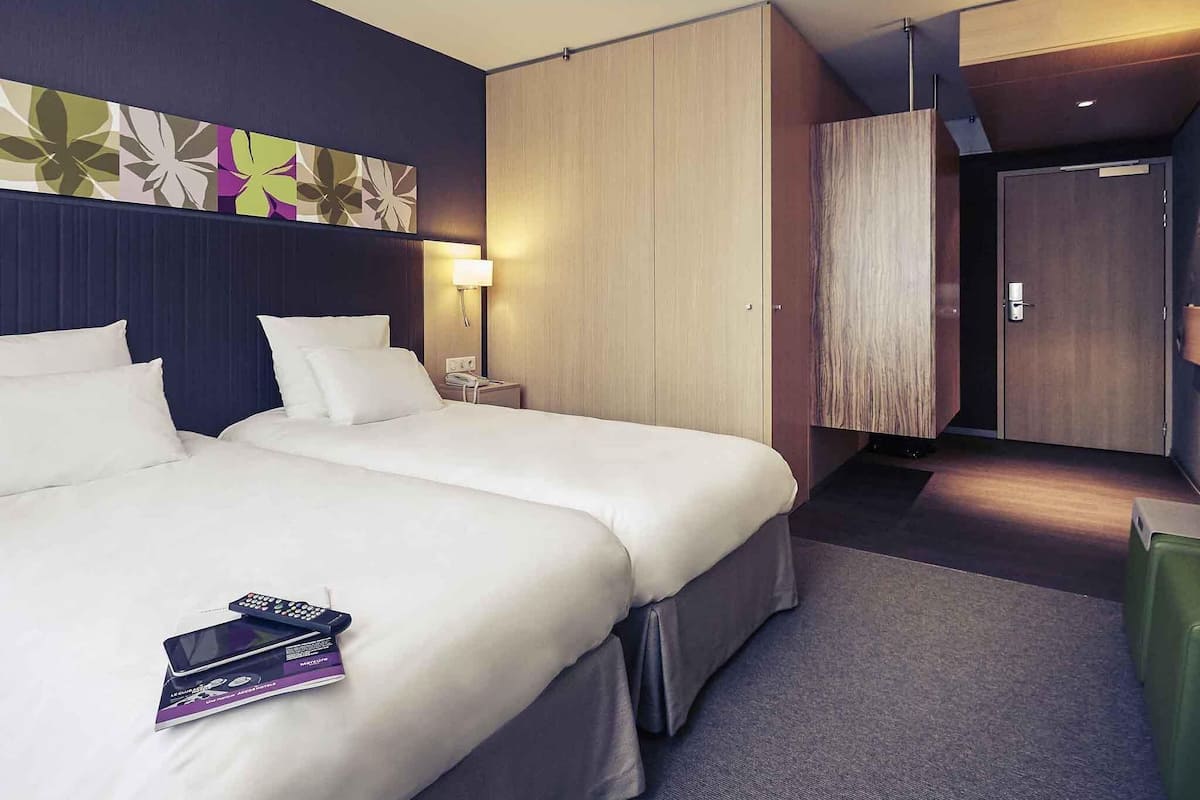 Een hotelkamer met twee bedden, een bureau, een stoel, een lamp en een kledingkast.