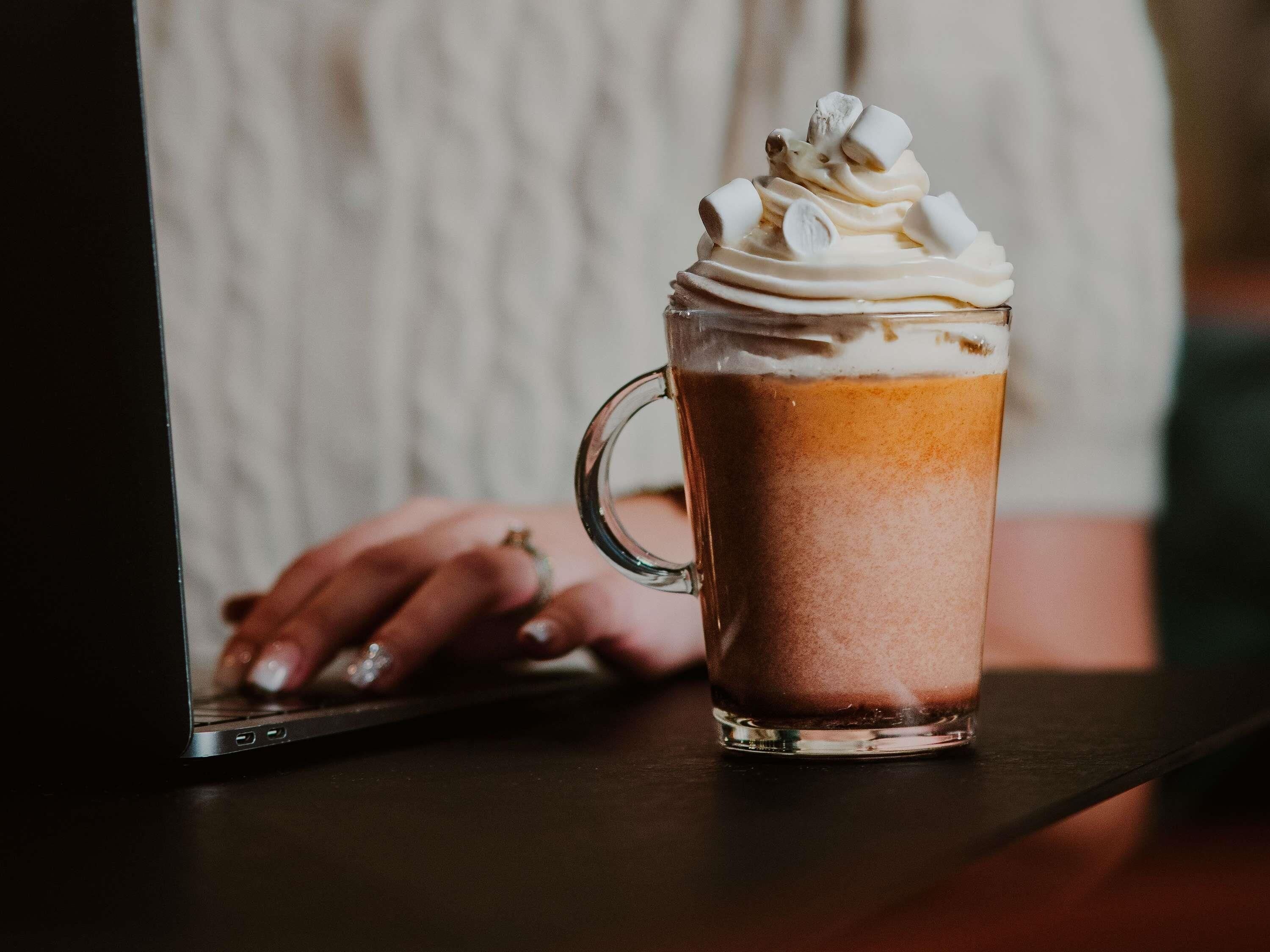 Une tasse en verre transparent contenant une boisson à plusieurs couches, peut-être un chocolat chaud ou un café, surmontée de crème fouettée.