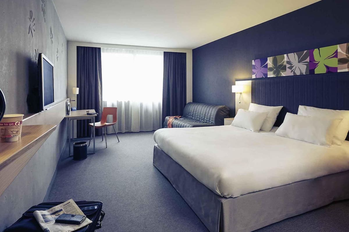 Een hotelkamer met een groot bed, een bureau met stoel, een televisie en een raam met gordijnen.