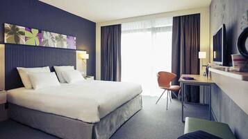 A hotel room with a bed, a desk, a chair, a TV, and a window with curtains.