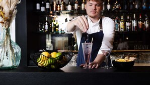 Un barman prépare un cocktail dans un bar, avec une variété de bouteilles visibles en arrière-plan.
