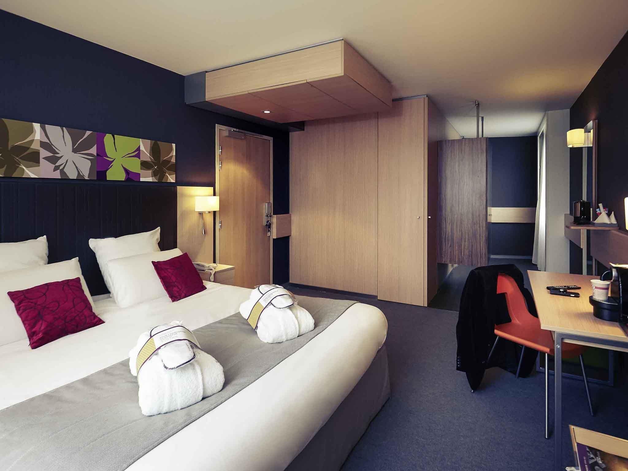 A modern hotel room with a large bed, a desk, and a wardrobe.