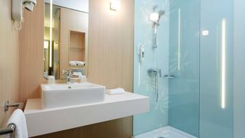 A modern bathroom with a white sink, a mirror, a glass shower enclosure, and a towel rack.