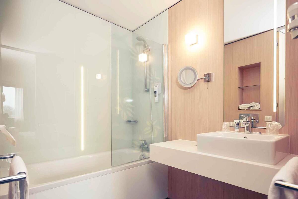 A modern bathroom with a glass-enclosed shower, a vanity with a mirror, and a wooden panel wall.