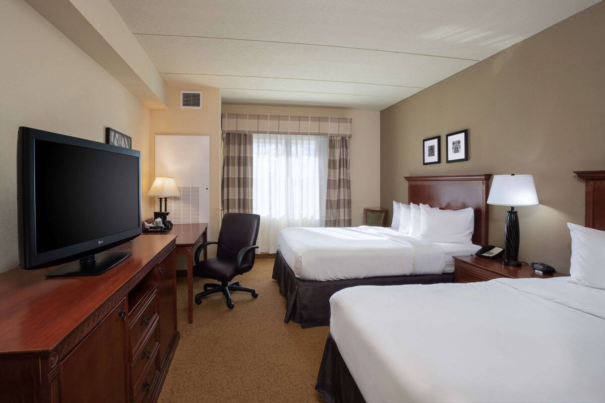 A hotel room with two beds, a TV, a desk with a lamp, and a chair.