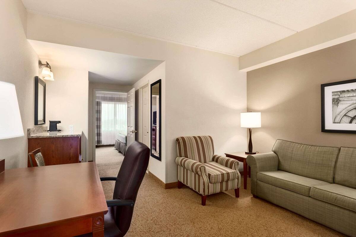 A hotel room with a wooden desk, a striped armchair, a green sofa, and a framed picture on the wall.