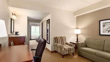 Habitación de hotel con un escritorio de madera, un sillón a rayas, un sofá verde y un cuadro en la pared.