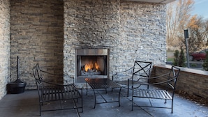 An outdoor seating area with stone walls, a fireplace, and metal chairs. - Country Inn & Suites by Radisson, Buffalo South I-90, NY (Buffalo)